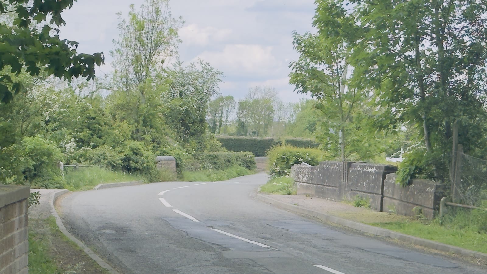 Quiet country road bending over a stone bridge between leafy trees